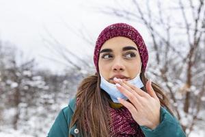 inte Rör din ansikte, sluta spridning coronavirus. ung kvinna rörande henne mun med smutsig hand. undvika rörande din ansikte. kvinna sätta ner ansikte mask gnuggning henne läpp utomhus. foto