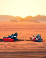 ung caucasian par lägga koppla av på sand tillsammans håll hand i kärlek Kolla på solnedgång i öken- utomhus i wadi rom utomhus i jordan. resa utforska samhörighet i muslim Land foto