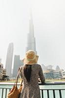 dubai, uae, 2022- modern turist kvinna resande ser på burj khalifa torn mot dimmig vit himmel, dubai, uae foto