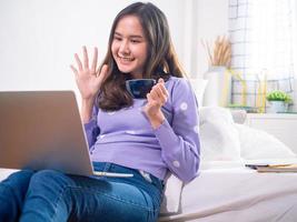 förbindelse av teknologi och modern sätt av tänkande de flicka vinkade hans hand till hälsa henne vänner via internet video kallelse , sitter och drycker kaffe i en avslappnad sätt. social distans begrepp foto