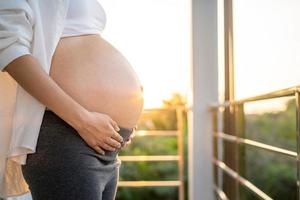 ett 8 månad gravid kvinna försiktigt finputsning henne mage på solnedgång. mamma med bebis i abbomen så Lycklig tid medan hon är gravid. foto