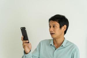 asiatisk man är chockade medan ser på en mobil telefon. män do ansiktsbehandling uttryck, överraskning meddelanden eller saker den där dyka upp på deras telefoner. foto