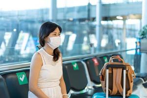 Asiatiska kvinnor bär en mask och sitter mellan stolarna för att minska spridningen av coronaviruset. turister väntar på att komma på flygplan under utbrottet av covid-19. foto