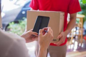 en kvinna är signering namn på en smartphone till motta en paket från leverans man. beställa Produkter uppkopplad med snabb leverans. foto