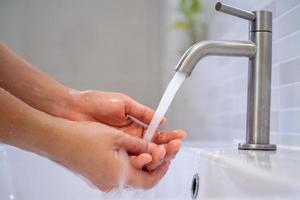 kvinnor sväng på de vatten till tvätta deras händer i de badrum. frekvent hand tvättning till hjälp rena, minska de ackumulation av bakterie och virus. foto