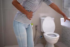 kvinna med diarre stående i de badrum, innehav henne mage. svår mage smärta, förbereda till sitta dynga i de badrum foto