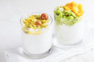 närbild två glasögon med yoghurt och färsk frukt puré är stående på vit tabell. foto
