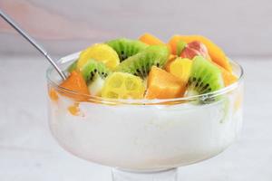 närbild glas skål på stam med yoghurt och skivad färsk frukt på vit bakgrund. foto