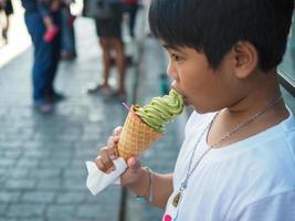 en pojke bär en vit skjorta är äter is grädde. foto