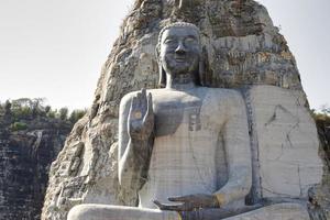 de skönhet och nåd av de sten buddha staty ristade från de klippor av de klippig fjäll, stor religiös arkitektur för dyrkan och turism, buddha staty Sammanträde på de knackar foto