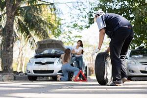 expertis mekaniker man i uniform med våld försöker skruva loss hjulbultarnas muttrar och hjälpa en kvinna för att byta bilhjul på motorvägen, bilservice, reparation, underhållskoncept. foto