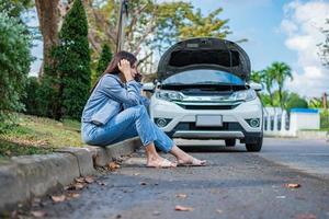 asiatisk kvinna sitter bredvid bilen efter ett bilhaveri på gatan. koncept av fordonsmotorproblem eller olycka och nödhjälp från professionell mekaniker foto