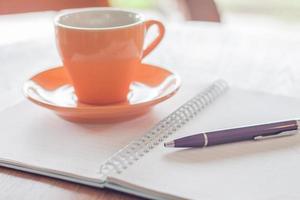 kaffekopp, en penna och en anteckningsbok på ett träbord foto