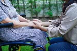 läkare hjälpa asiatisk äldre kvinna funktionshinder patient sitter på rullstol i parken, medicinsk koncept. foto