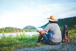 en senior asiatisk kvinna är bär en hatt Sammanträde på de gräs till ser en Karta av natur turism. de begrepp av hälsa turism för de äldre foto