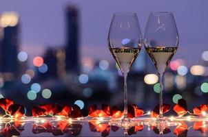 två glasögon av vit vin på tabell med ljus och hjärta papar vika ihop med färgrik bokeh ljus från stad bakgrund för valentines dining begrepp. foto