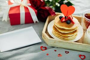 hemlagad pannkakor med bär, blommor och gåva låda. frukost eller brunch för hjärtans dag. mockup. tom för hälsning kort för text foto