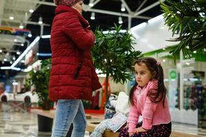 upprörd liten förlorat flicka Sammanträde på bänk i köpcenter foto