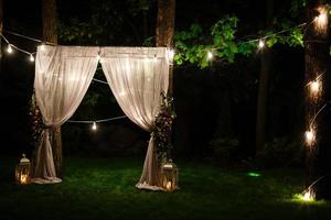 bröllop skymning ceremoni dekoration tillverkad av hängande på en träd gyllene lyktor och lampor och stående på de gräs sparken ljus med de matta i de mitten foto