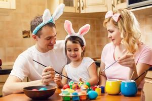 mor, far och dotter är målning ägg. Lycklig familj är framställning för påsk. söt liten flicka bär kanin öron. foto