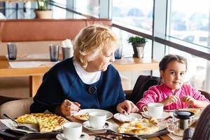 barndom och människor begrepp - Lycklig mormor och liten flicka med sked äter på utomhus- Kafé eller restaurang foto