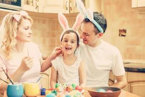 mor, far och dotter är målning ägg. Lycklig familj är framställning för påsk. söt liten flicka bär kanin öron. foto
