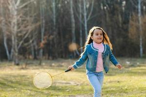 liten flicka i jeans spelar tennis i de parkera foto