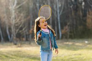 söt liten flicka spelar badminton utomhus på värma och solig sommar dag foto