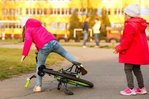 en liten flicka i säkerhet redskap, sitter i de mitten av en kör efter faller av henne ny cykel. foto