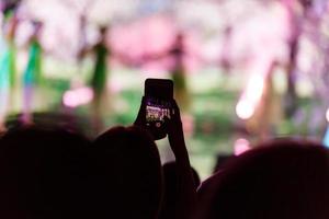 en smartphone hölls med två hand i beställa till skjuta en antal fot under en konsert. foto
