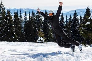 en skidåkare eller snowboardåkare står på en kulle eller en backe på en bakgrund av bergen täckt med skogar och snötäckt. de lura runt om och skrattande, Lycklig och glädjas foto