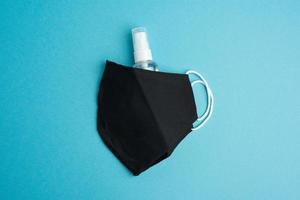återanvändbar svart textil- mask, flaska för desinfektor på en blå bakgrund foto