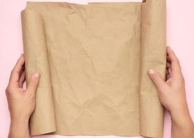 två manlig händer håll en rulla av brun papper på en rosa bakgrund foto