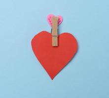 röd papper hjärta fästs på en trä- klädnypa, blå bakgrund foto