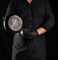 manlig laga mat i svart enhetlig och latex handskar innehar ett tömma runda årgång svart kasta järn panorera i främre av honom foto