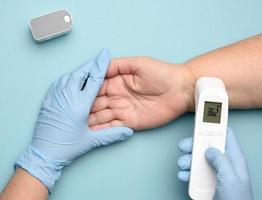 läkare i blå latex handskar åtgärder de temperatur med ett elektronisk kontaktlös grej foto