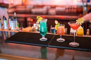 exotisk cocktails, mojito cocktail, orange cocktail, jordgubb cocktail i glas glasögon med strån och frukt och suddig bar Tillbehör shaker, sked, kryddor färgrik cocktails på de bar disken foto