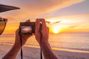 man innehav kamera, tar Foto av sommar strand. fotografer eller resenärer använder sig av en professionell dslr kamera ta Foto skön solnedgång landskap, fredlig strand solnedgång.