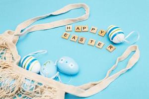 inskrift Lycklig påsk med färgrik målad ägg och bomull sträng väska på blå bakgrund foto