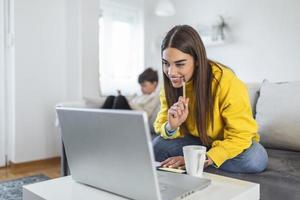 göra flera saker samtidigt mor arbetssätt från Hem. moms kan balans arbete och familj. mor och son använder sig av teknik på tabell. familj är arbetssätt på bärbar dator och digital läsplatta på Hem. foto