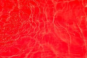 defokusering suddig transparent röd färgad klar lugna vatten yta textur med stänk och bubblor. trendig abstrakt natur bakgrund. vatten vågor i solljus med kaustik. röd vatten glänsande foto