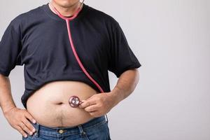 medicinsk kolla upp upp begrepp fett människor innehav röd läkare stetoskop för kolla upp hans hälsa och kropp. studio skott på grå foto