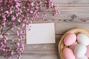 rosa blommor, en bo med ägg i mjuk pastell färger och tom vit kort för text på en trä- bakgrund. mockup. plats för text. påsk kort foto
