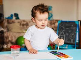 en små pojke sitter på en stol och drar med färgad målarfärger foto