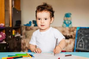en söt liten pojke drar i hans skissbok med färgad pennor foto