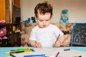 en söt liten pojke drar i hans skissbok med färgad pennor foto