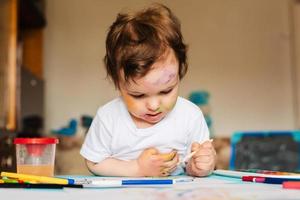 en små söt pojke målarfärger med borstar och färgad målarfärger på en ark av papper foto