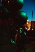 ung flicka i total svart innehar svart ballonger på de gata foto