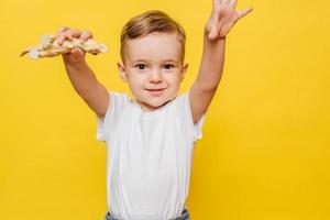 söt skrattande liten pojke på en gul bakgrund med en dinosaurie leksak i hans händer. foto