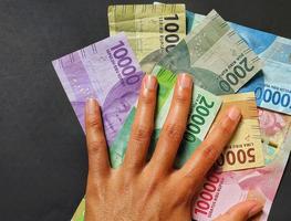 en person innehav kontanter i indonesiska rupiah sedlar isolerat på svart bakgrund foto
